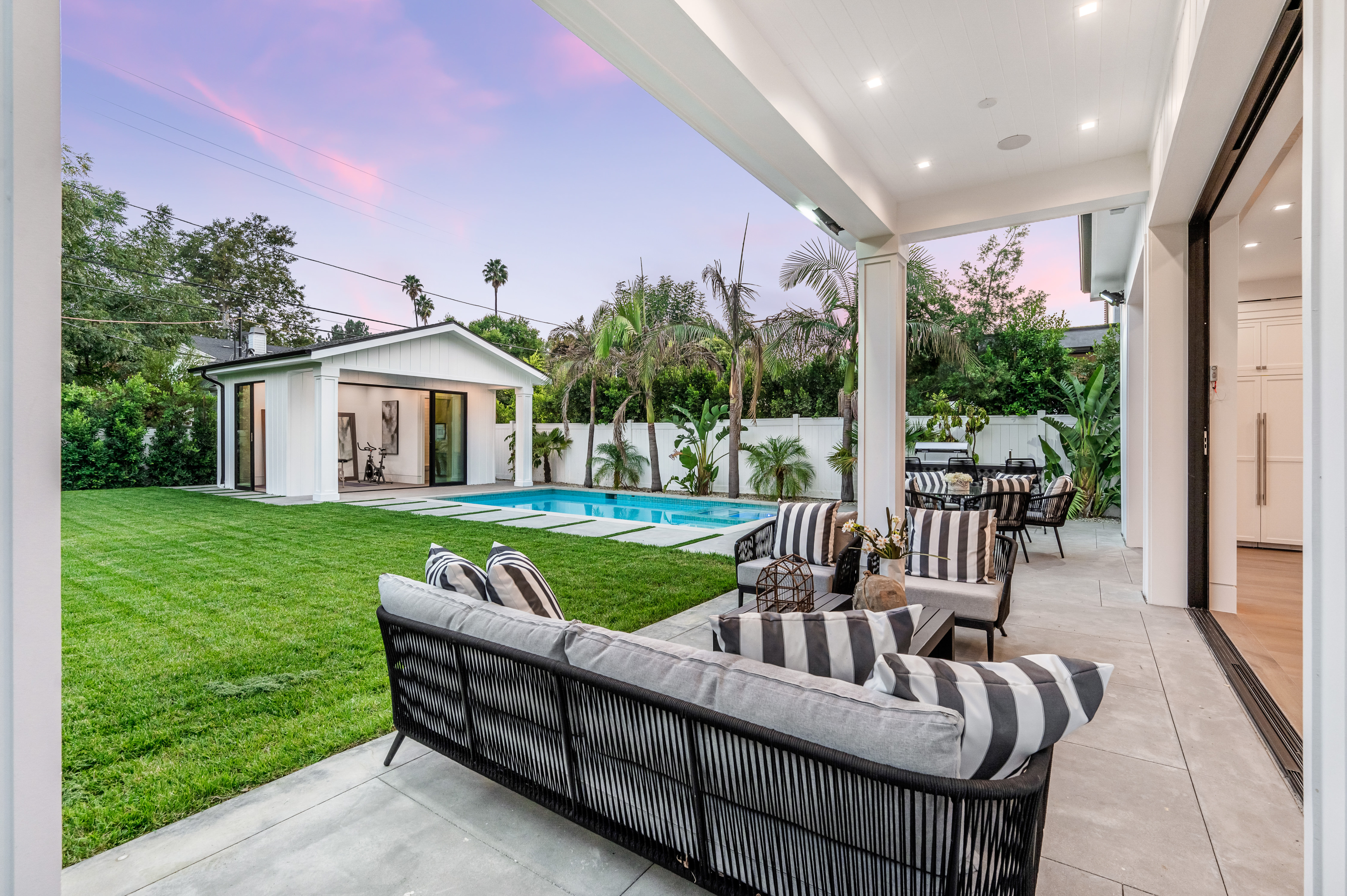 Backyard lounge with pool, lush landscaping, and covered patio at dusk