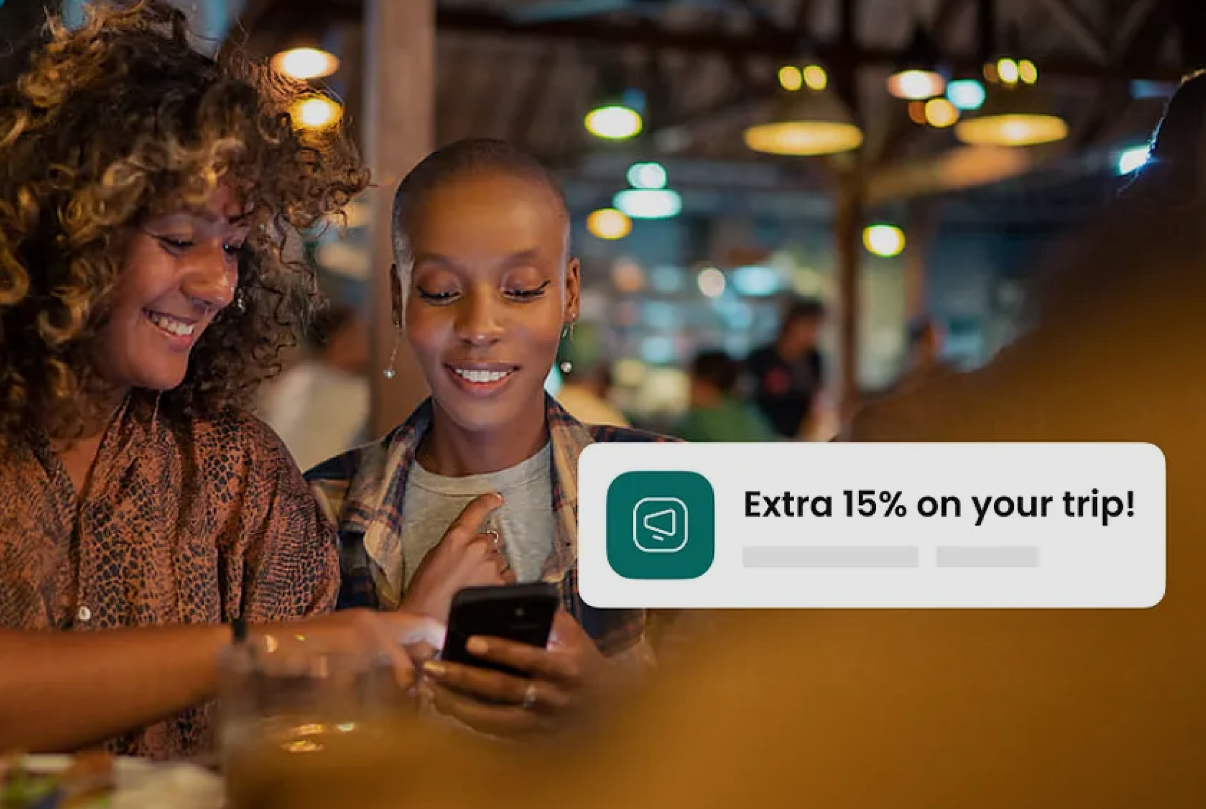 Two women smiling at a smartphone in a warmly lit restaurant